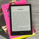 The Amazon Kindle Paperwhite 5 sitting atop a pile of books on a desk.